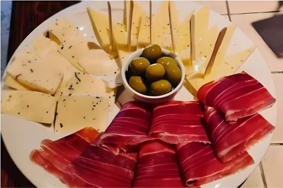 A plate of ham, sliced cheeses and olives, arranged elegantly with wooden picks for a classic Mediterranean appetizer.