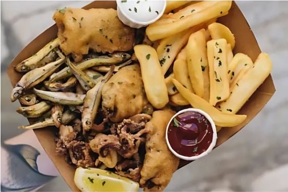 A hearty seafood platter with fried fish, crispy calamari, fries, and dipping sauces, garnished with lemon wedges.