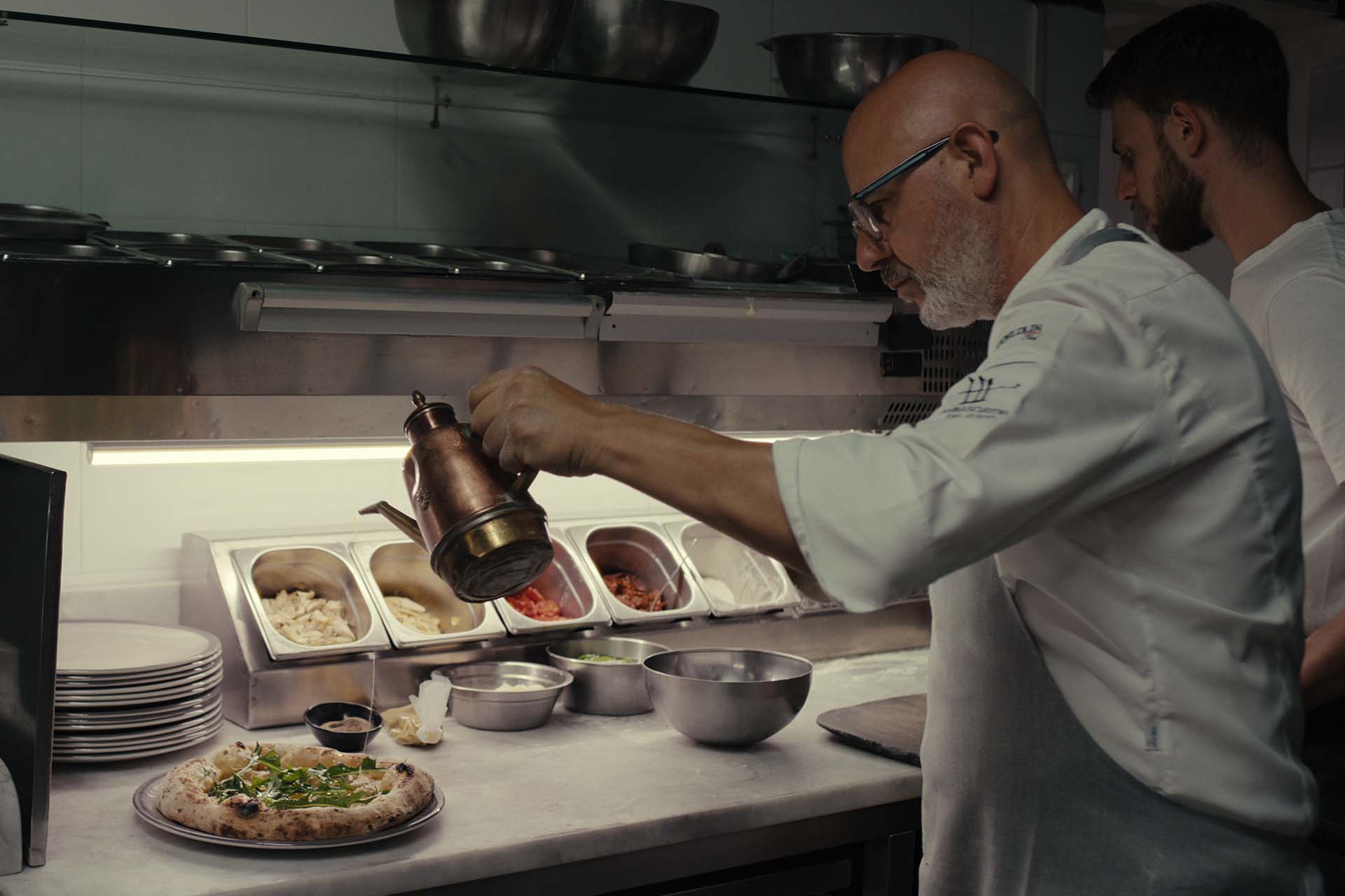 A man pouring oil on a pizza.