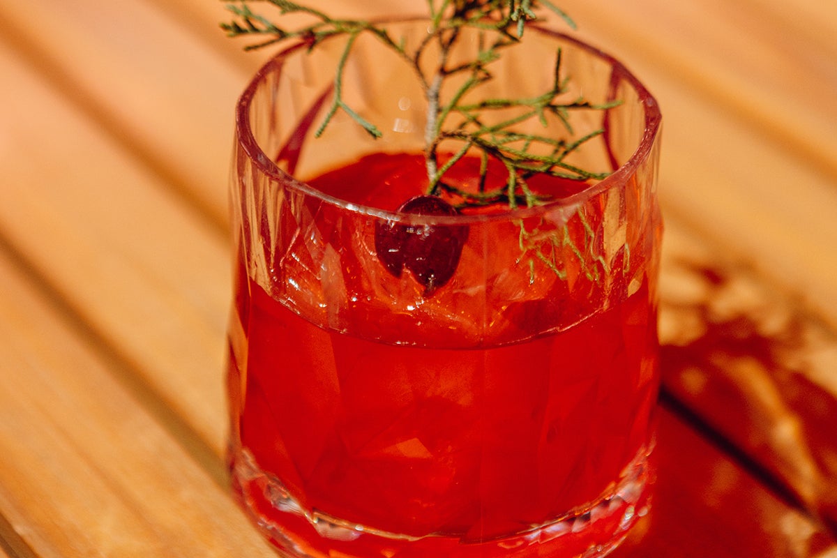 red cocktail in glass on table with sprig of pine