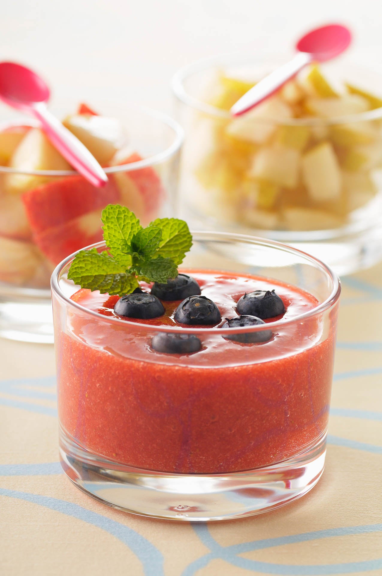 Glass of strawberry gazpacho topped with mint and blueberries.