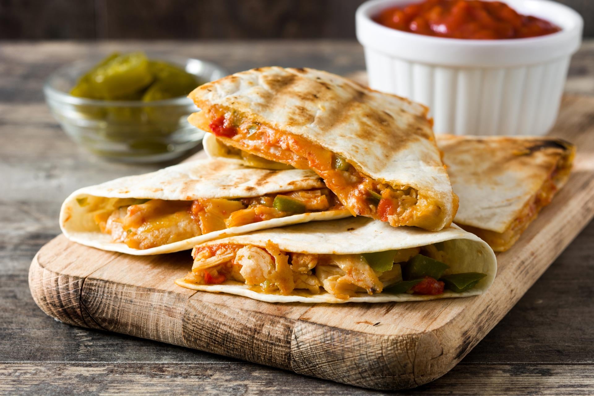 Chicken quesadillas on a board with condiments.