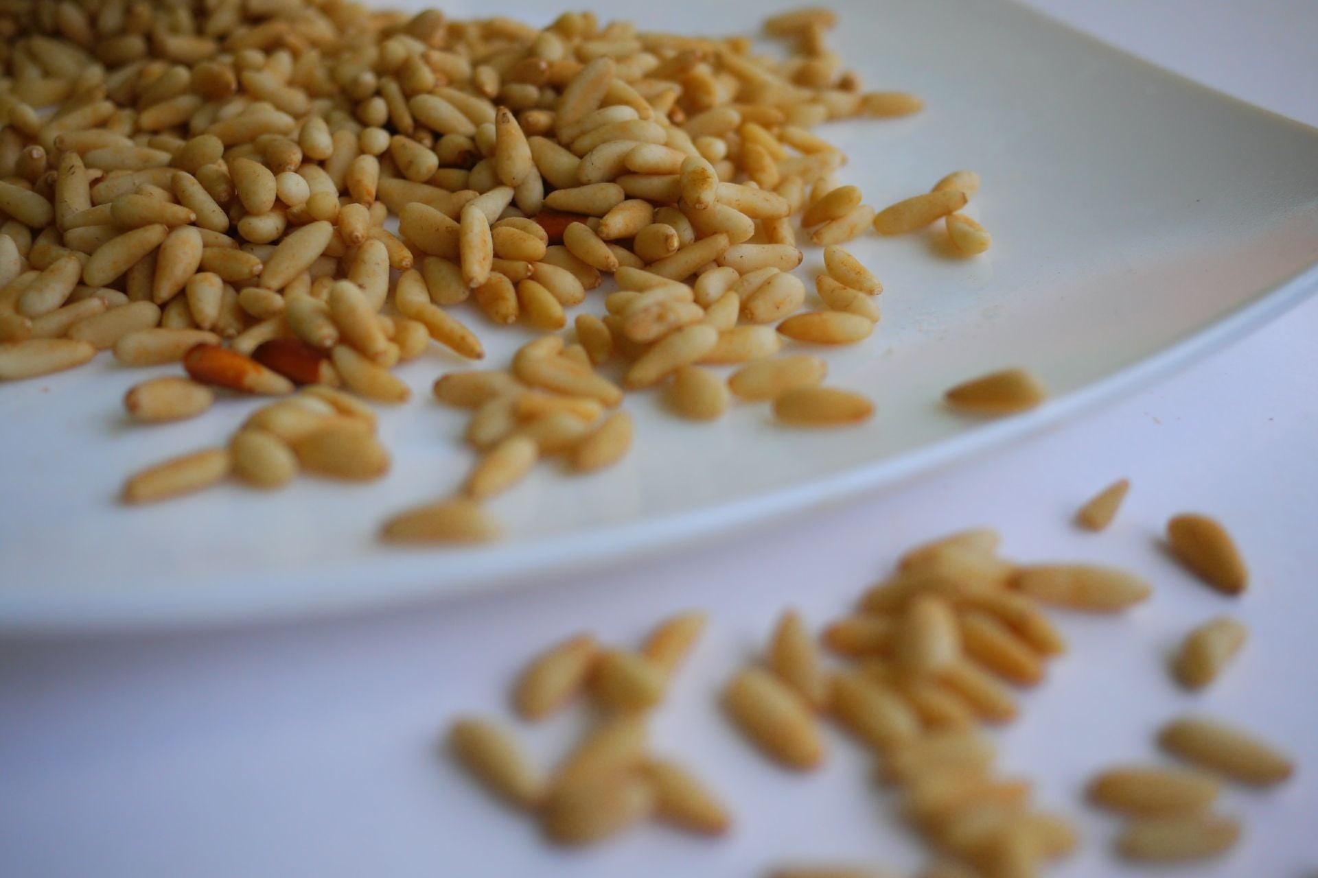 pine nuts spilling off a plate onto a white table top