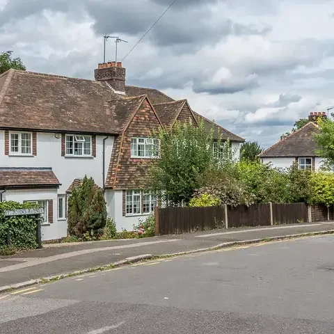Charming British homes with brick chimneys and neatly trimmed gardens, set along St. Johns Avenue under a cloudy summer sky