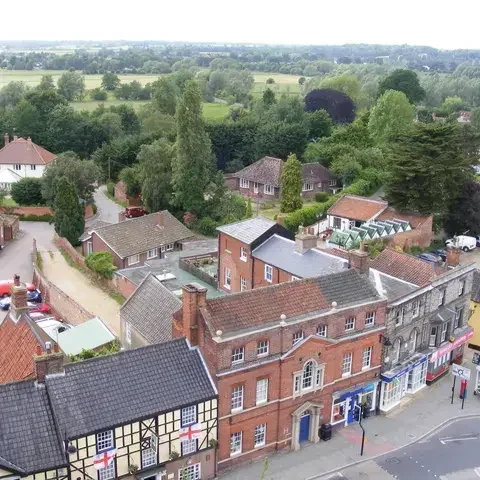 View of an English town with red brick houses, greenery, and fields stretching into the distance under a cloudy sky