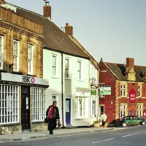 Historic town street with HSBC bank, pastel-colored buildings, and Red Lion pub in warm evening light