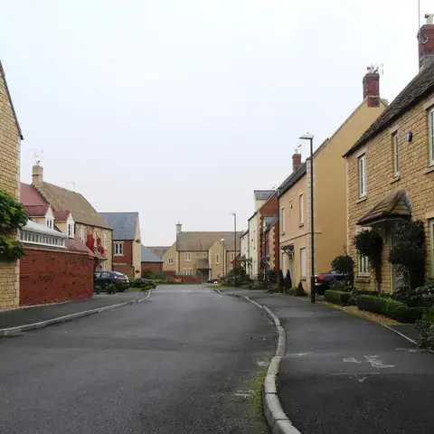 Stone houses line a quiet residential street with manicured greenery, creating a peaceful village ambiance