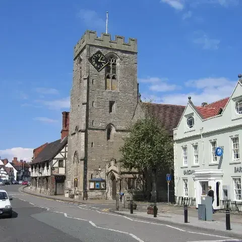 Historic church tower and village street in Henley-in-Arden, under a bright blue sky with charming architecture