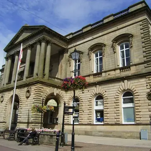 Elegant stone town hall with classical columns and hanging flower baskets, set under a bright blue sky