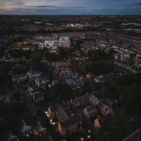 Aerial view of a quiet town at dusk, with glowing streetlights, dark rooftops, and the horizon fading into the evening sky.