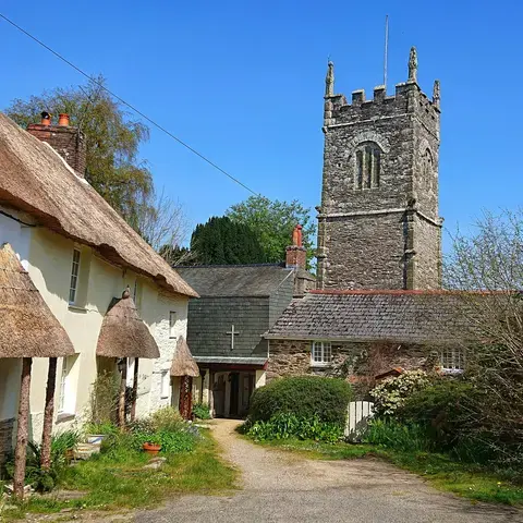 Traditional English village scene with thatched cottages and a historic stone church tower under a clear blue sky