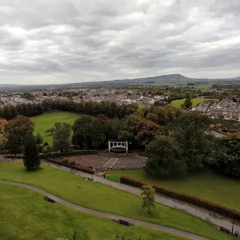 Overlooking a lush park with an amphitheater, nestled among a quiet town and rolling hills under a cloudy sky