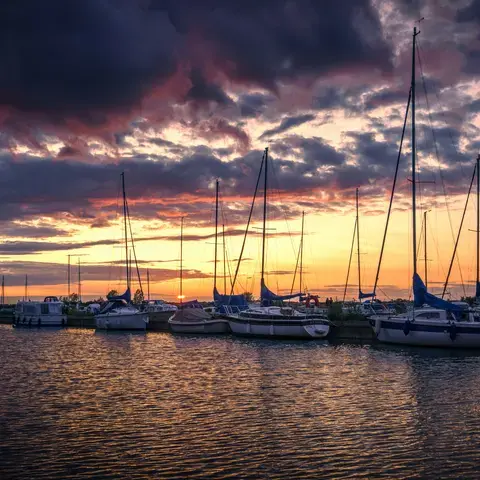 Serene marina at sunset with yachts silhouetted against vibrant orange and purple skies, reflecting on calm water