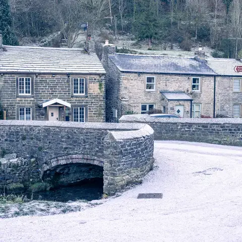 Snow-dusted stone cottages and a bridge over a small stream in a quaint winter village setting