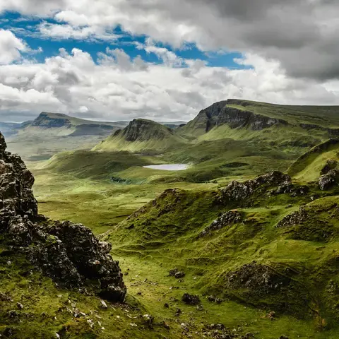 Rolling green hills and dramatic cliffs of Scotland’s Quiraing under a cloudy sky, a serene and rugged Highland landscape