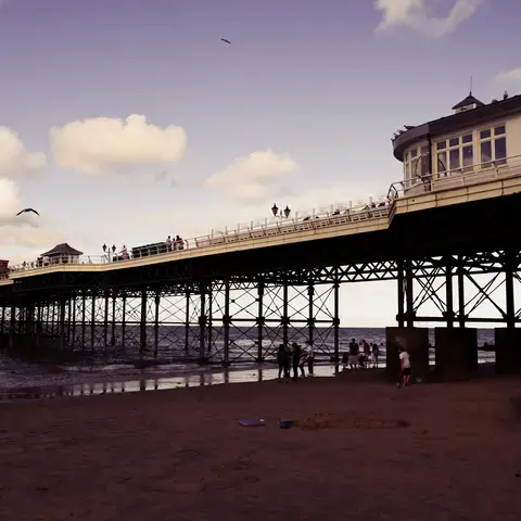 Victorian pier stretching over the sea,with Pavilion Theatre and visitors enjoying a seaside stroll under a purple-tinged sky
