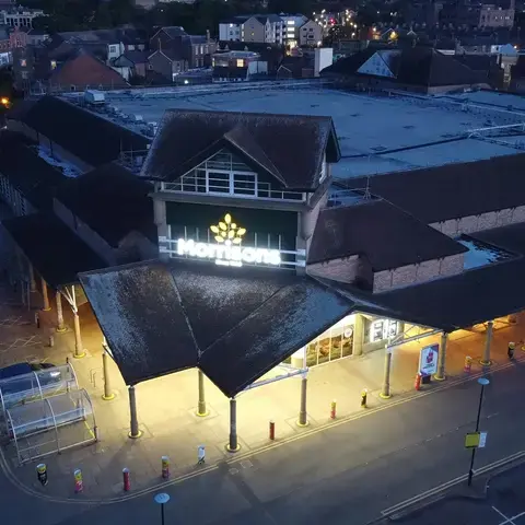 Exterior view of a Morrisons supermarket at dusk, with illuminated signage and empty parking area