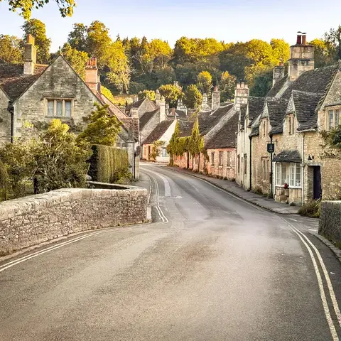 Charming English village road with stone houses, ivy-clad walls, and lush greenery, illuminated by golden evening sunlight