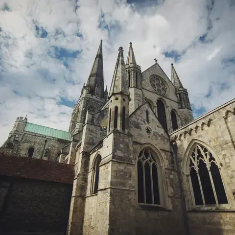 Gothic cathedral with spires and arches under a cloudy sky, showcasing intricate stonework and historic architecture