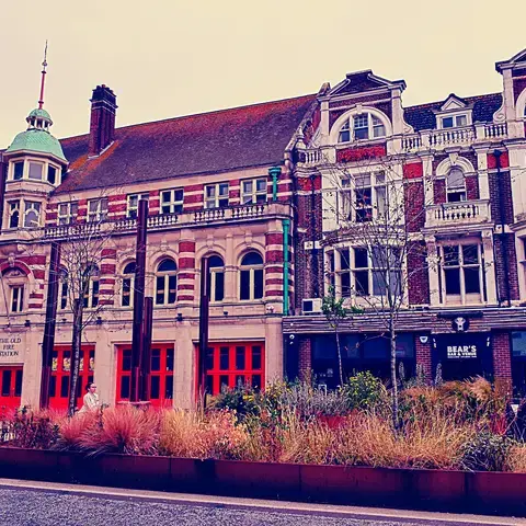 Historic red-brick building with arched windows and a green dome. Bright red doors highlight the old fire station’s character