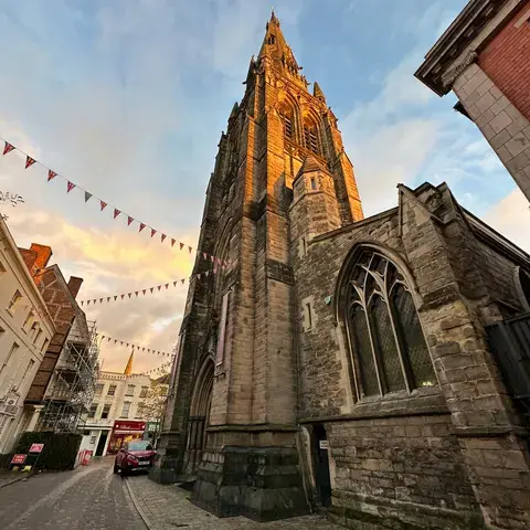 Gothic church tower glowing in sunset light, cobbled street below, festive bunting adds charm to the scene