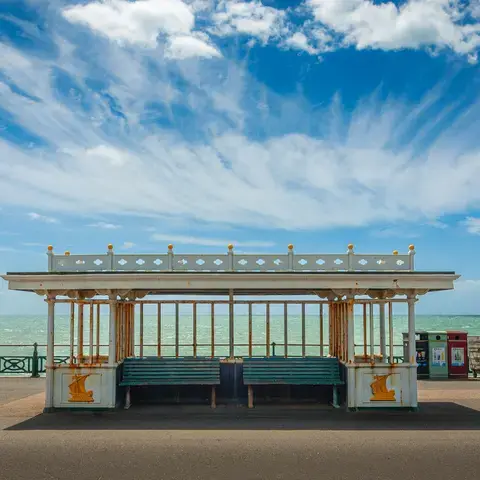 Seaside promenade with a vintage shelter, turquoise sea, and a bright blue sky with wispy clouds