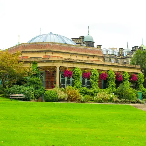 Elegant domed pavilion with lush greenery and vibrant hanging flowers,set in a peaceful park with benches and well-kept lawns