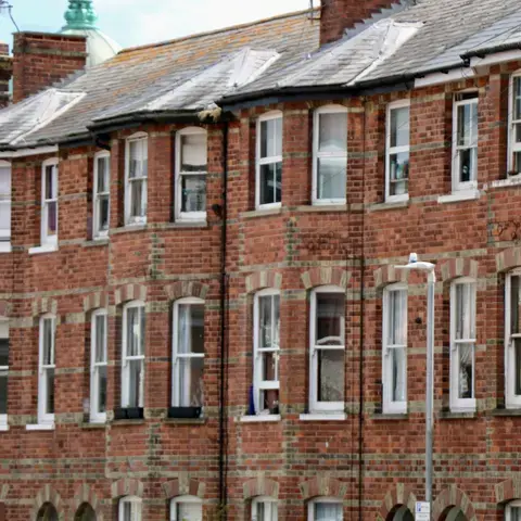 Brick apartment building with multiple windows and arched accents, under a cloudy sky