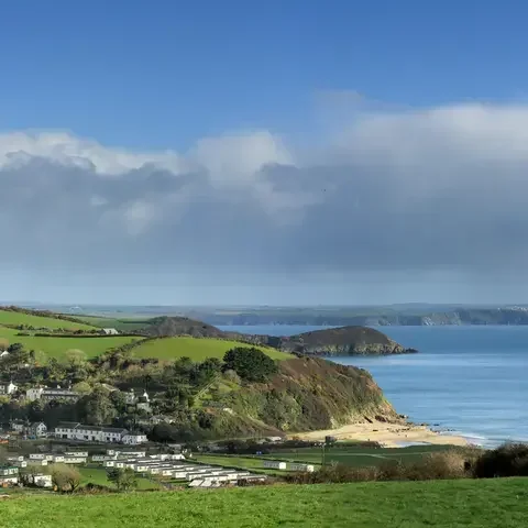 Scenic coastal landscape with a small village nestled among green hills overlooking a calm blue sea under a partly cloudy sky