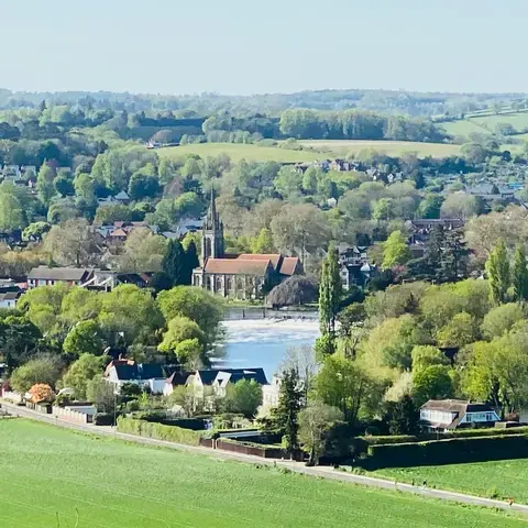 Serene village with a church, green fields, trees, and hills in the distance under a bright, clear sky
