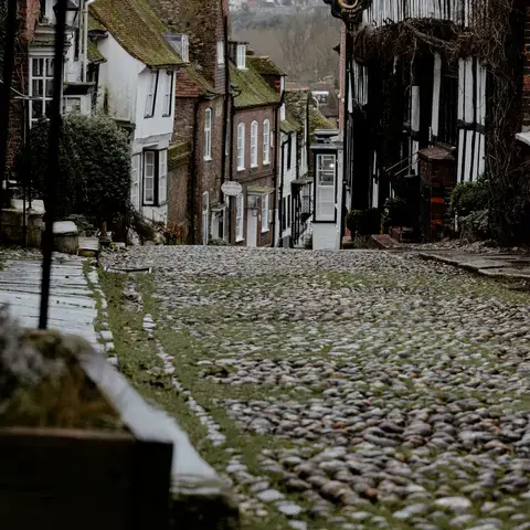 Quaint cobblestone street with mossy stones, historic timber-framed houses, and a gray overcast sky in a hillside village