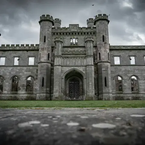 Ruined Gothic-style castle with tall towers and arched windows under a dramatic cloudy sky.
