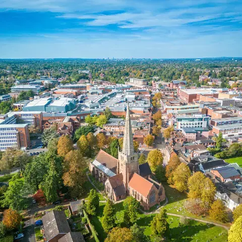 An aerial view of a bustling town with a historic church in the foreground, surrounded by greenery and modern buildings