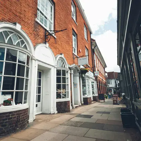 Narrow street lined with red brick buildings and white-framed shop windows, reflecting a quaint and charming town ambiance