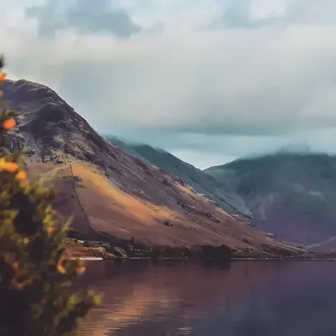 Mountain landscape reflected in a calm lake, with soft clouds and warm tones.