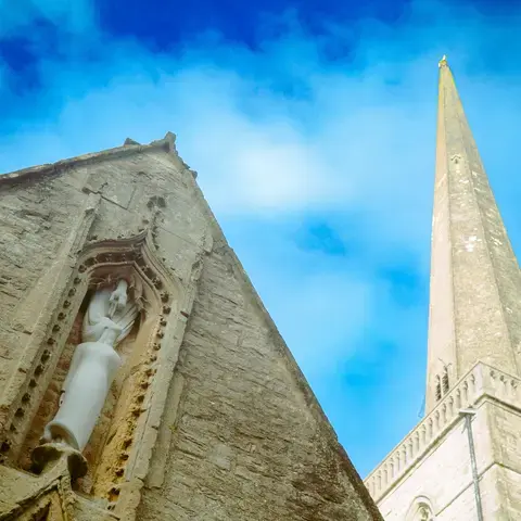 Close-up of a stone church with intricate sculpture detail, alongside its tall spire reaching into a bright blue sky