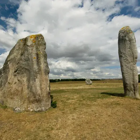 Ancient standing stones at Avebury henge, Wiltshire, surrounded by open fields, under a vast, cloud-filled sky