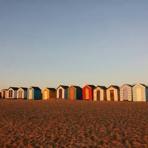 Colorful beach huts on golden sands, basking in the warm glow of a sunset under a clear evening sky