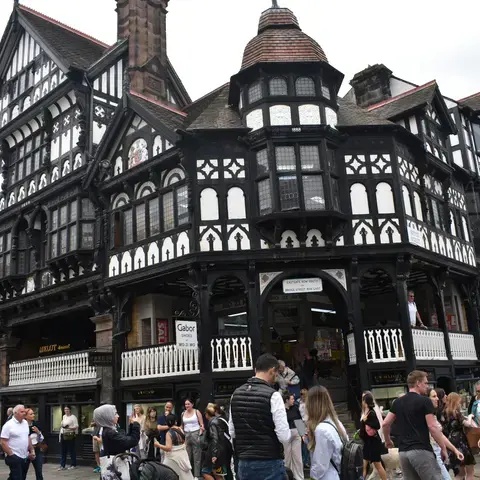 Crowd walking by a historic black-and-white timbered building, featuring intricate architecture and a vibrant atmosphere.
