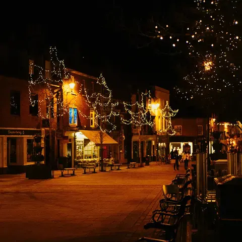 Town square at night with sparkling lights on trees and warm shopfronts, creating a cozy and festive atmosphere