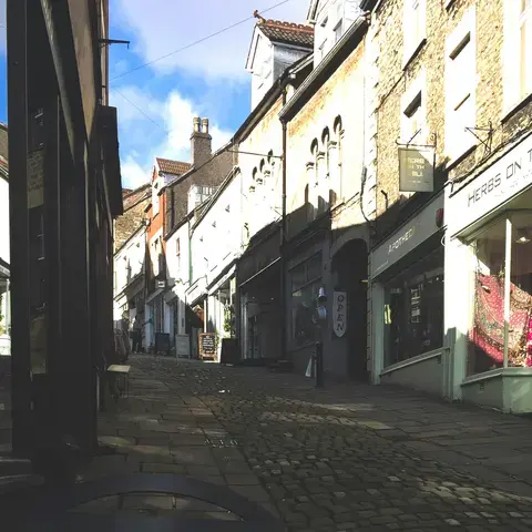 Charming cobblestone street lined with small shops and a sign reading ‘When in Frome’ promoting independent shopping