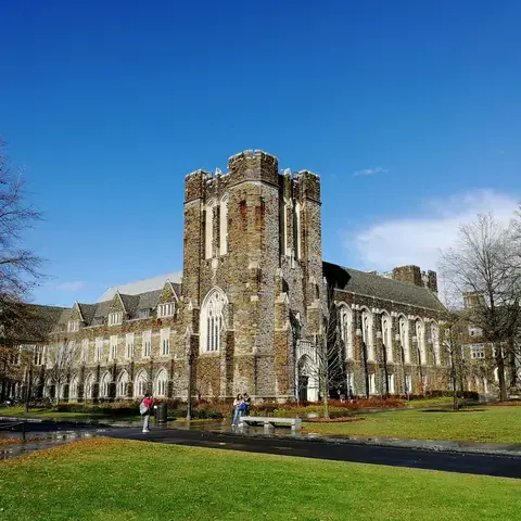 Gothic-style stone building with arched windows, central tower, green lawn, and blue sky.