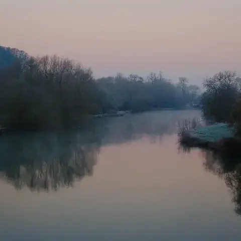 Peaceful river surrounded by frosty trees under a pastel pink and blue sky during dawn