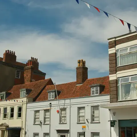 Charming townhouses with red brick chimneys under a bright blue sky, adorned with festive bunting in red, white, and blue