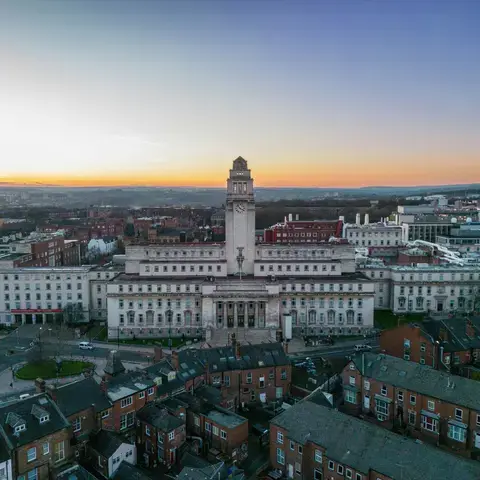 Sunset view of a historic university building, surrounded by city rooftops and modern architecture stretching to the horizon