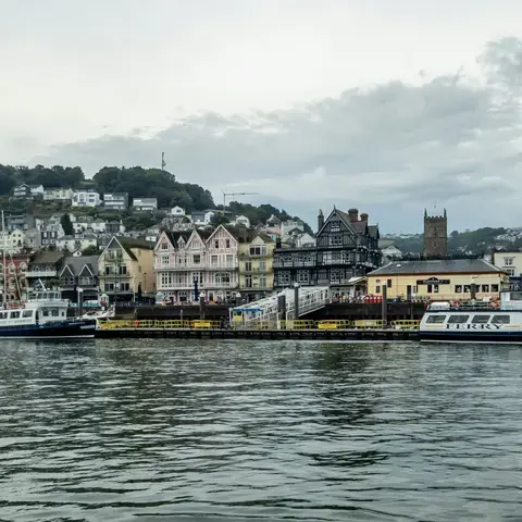 Charming waterfront town with pastel buildings, a historic black-and-white structure, and ferries docked by the scenic bay