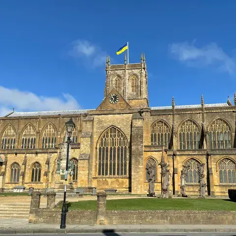 Historic stone church with tall arched windows and a clock tower flying the Ukrainian flag under a clear blue sky