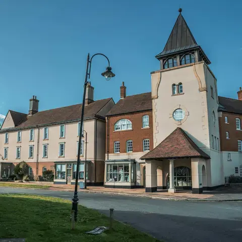 Charming village scene with a classic clock tower, quaint buildings, and lush greenery, all under a bright blue sky
