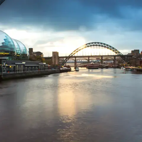 Evening view of a modern riverside with a glass dome building, iconic arched bridge, and reflections on the calm water
