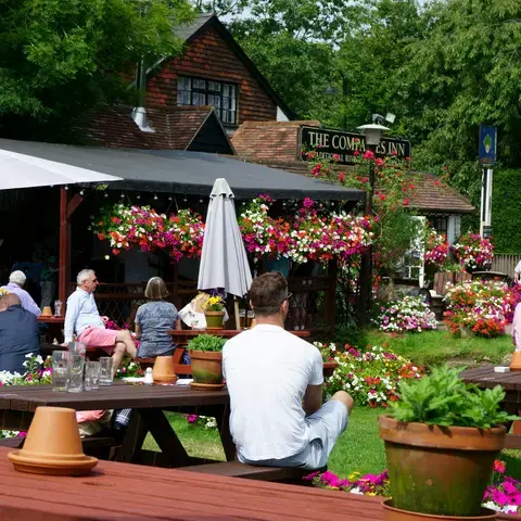 Pub garden with flowers, wooden tables, umbrellas, and people enjoying drinks in a sunny, cozy outdoor setting
